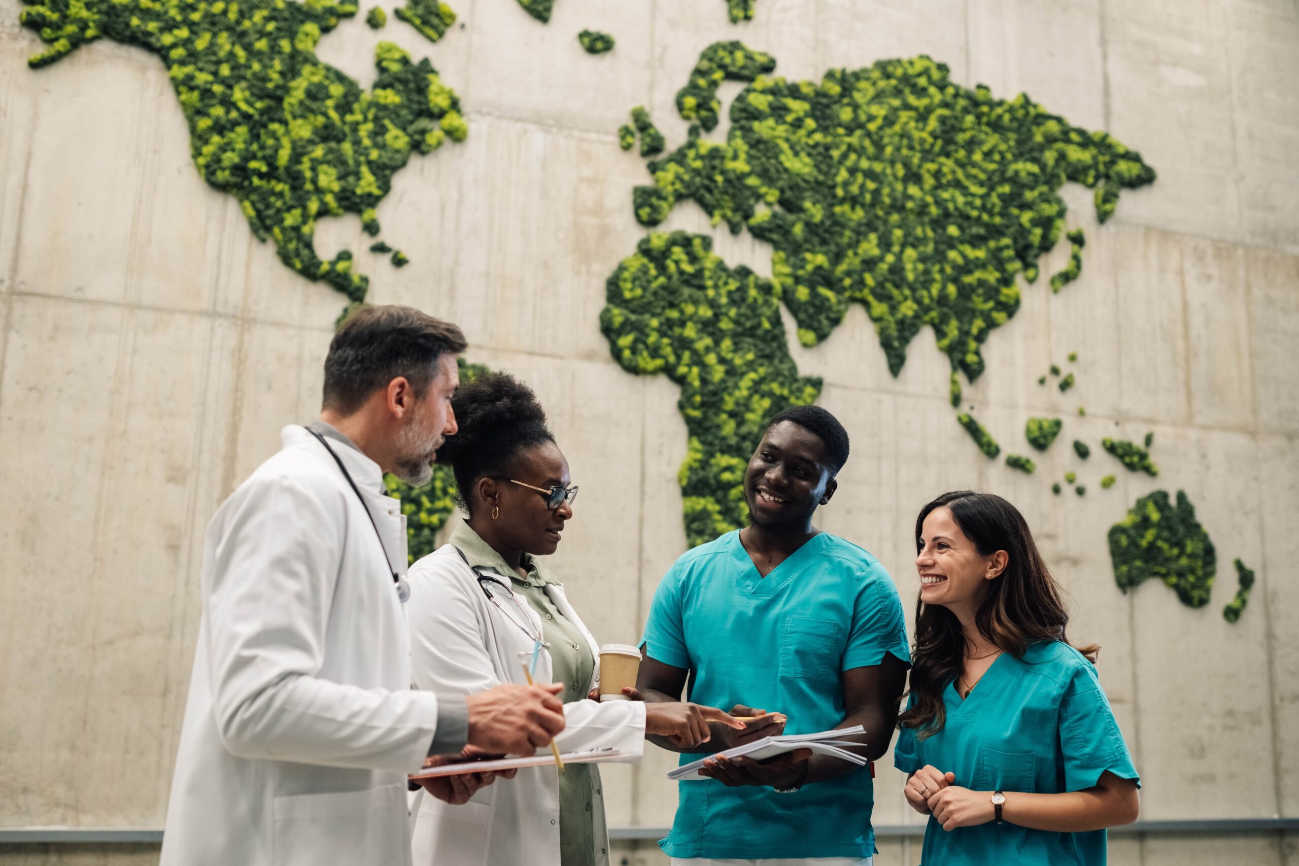 Healthcare workers talking in front of a wall showing a world map made of greenery, symbolizing sustainability in healthcare.