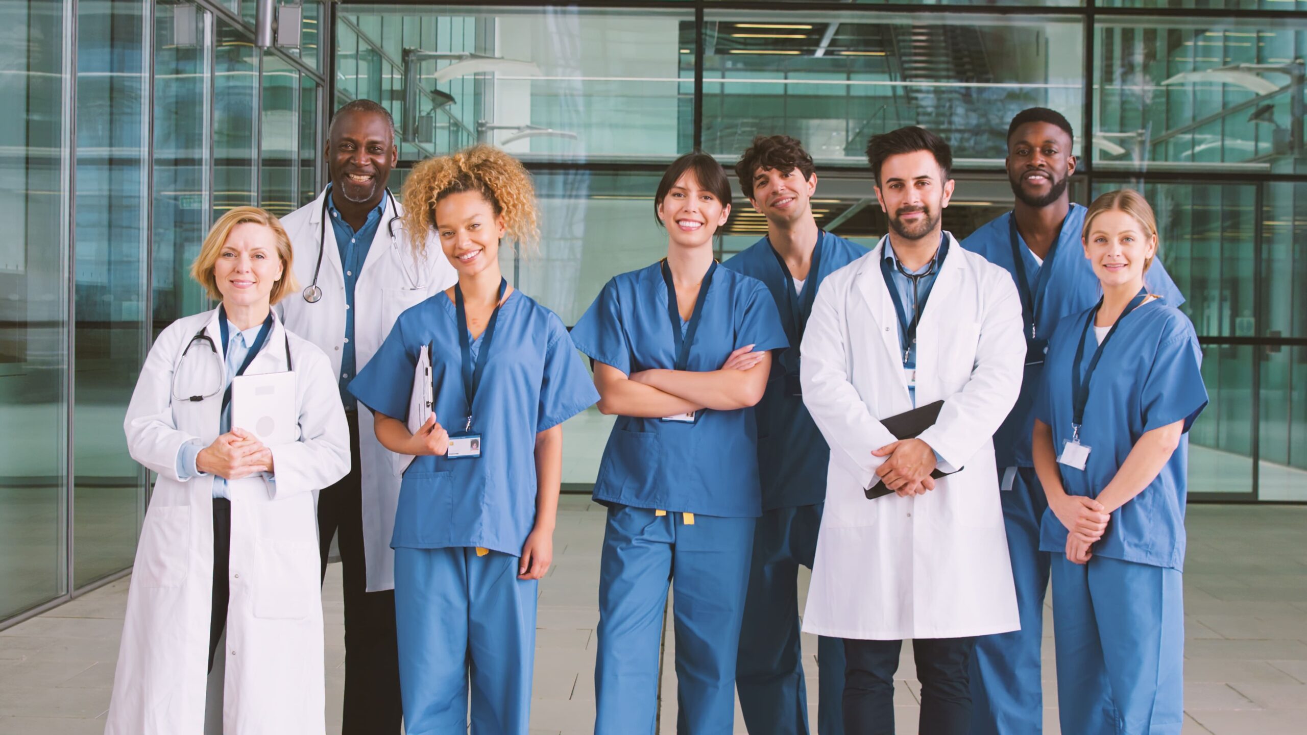 Group of nurses and doctors standing in a medical building, smiling and facing the camera.