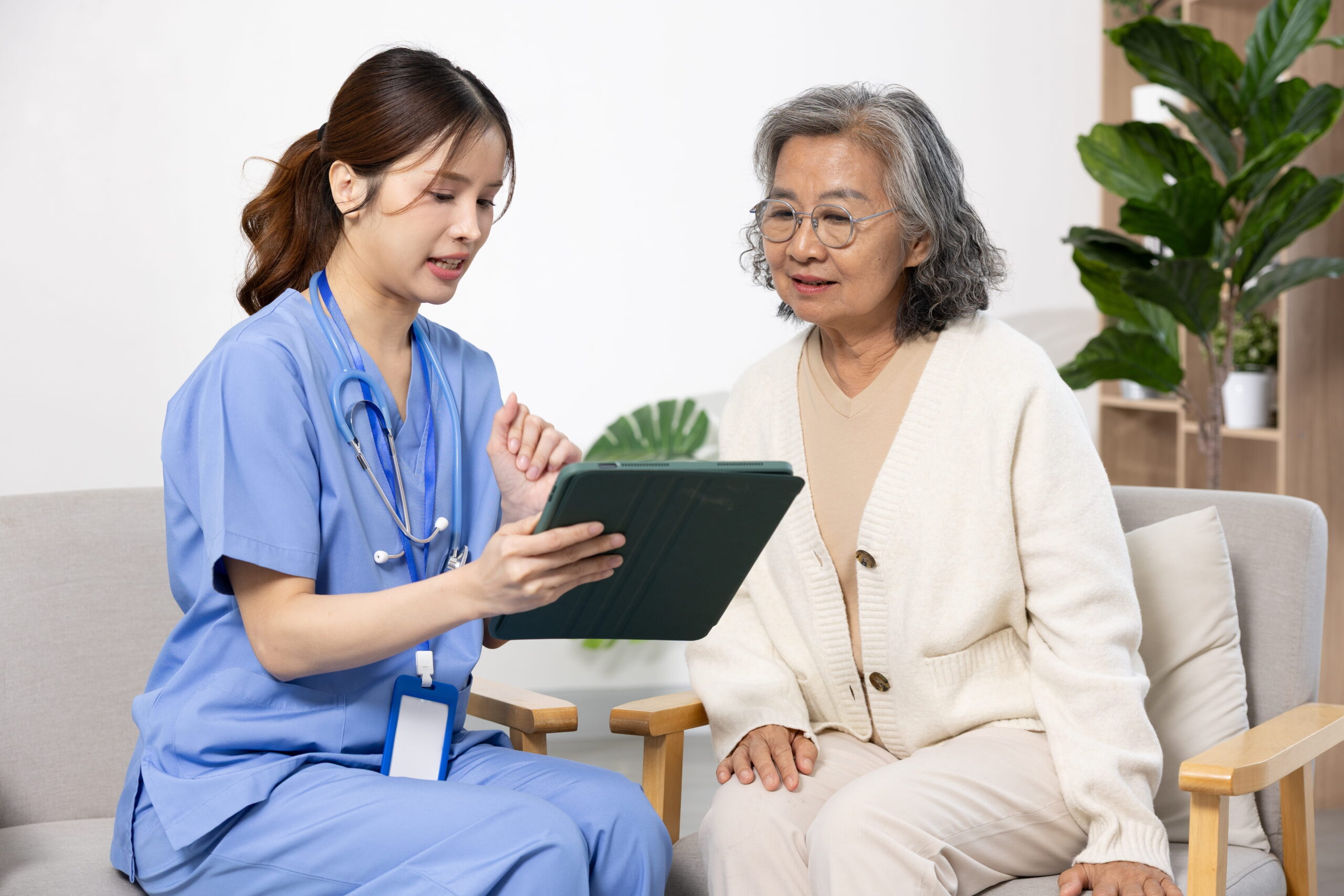 Nurse reviews medical information on a tablet with an older patient.