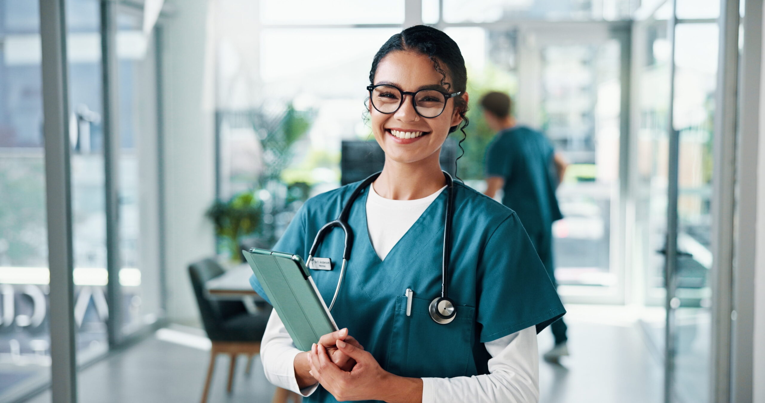 Smiling nurse with glasses holding a tablet in a healthcare facility, representing the benefits of earning a BSN degree and advancing a nursing career.