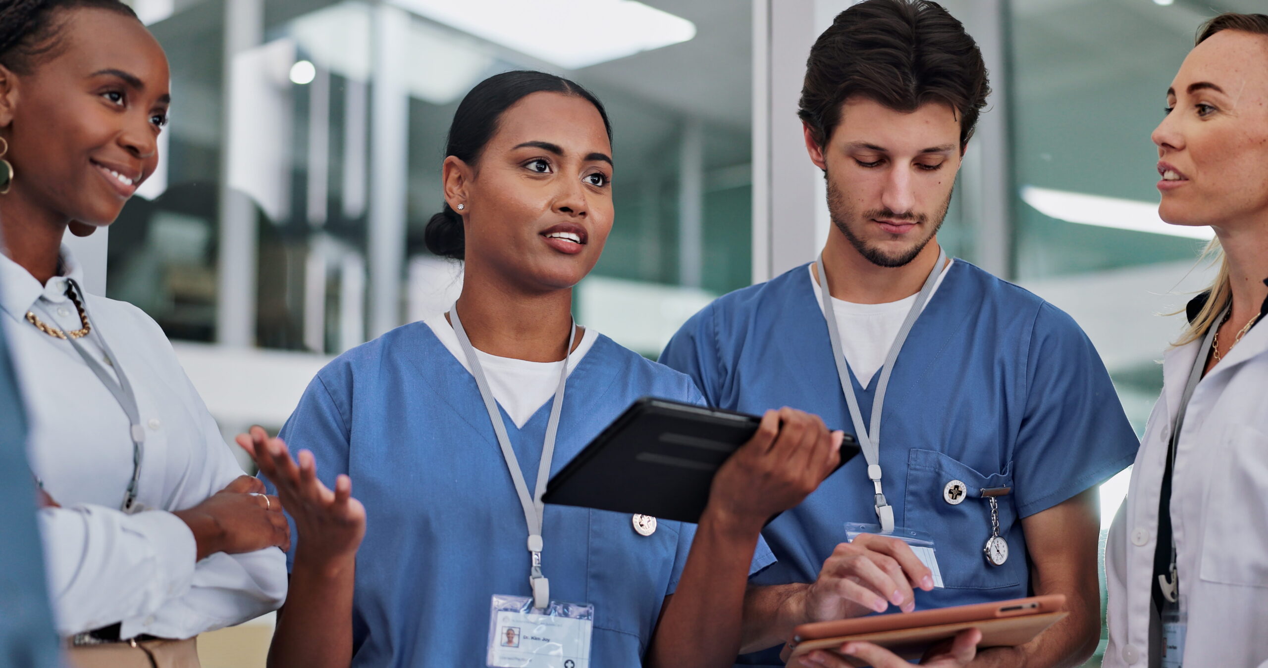 Group of nurses discussing patient information while using tablets in a healthcare setting.