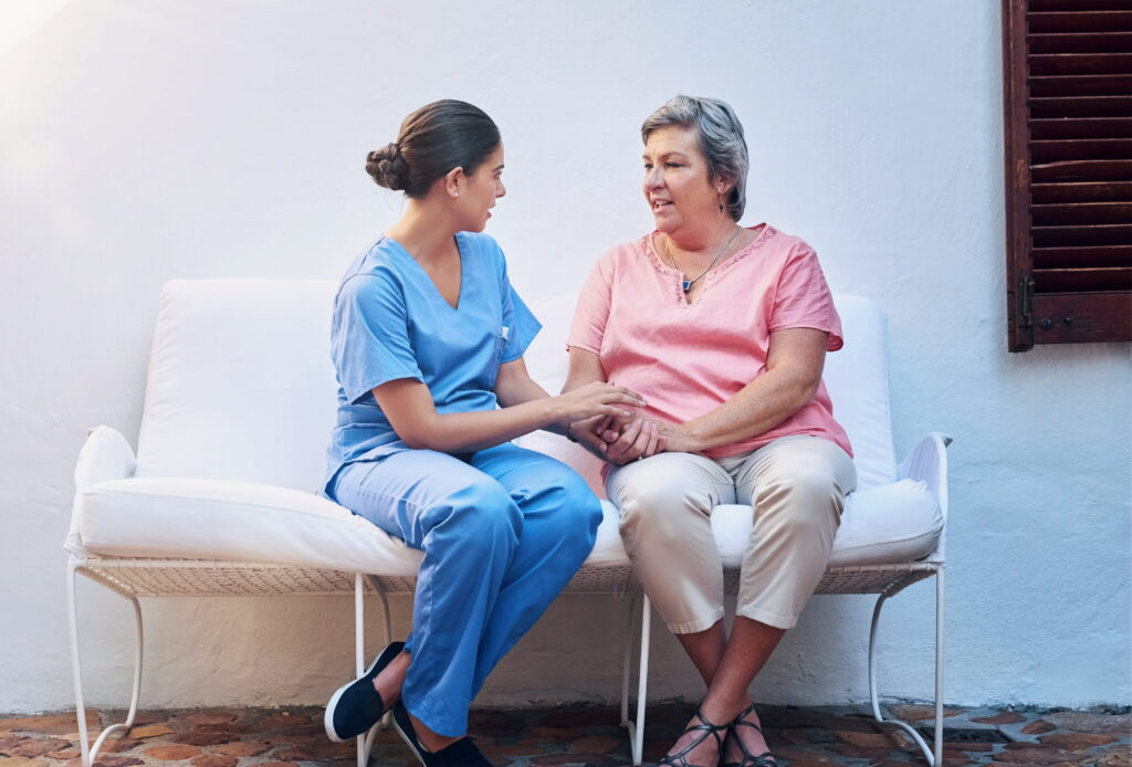 Nurse providing compassionate support and communication while speaking with an older patient in a home care setting.