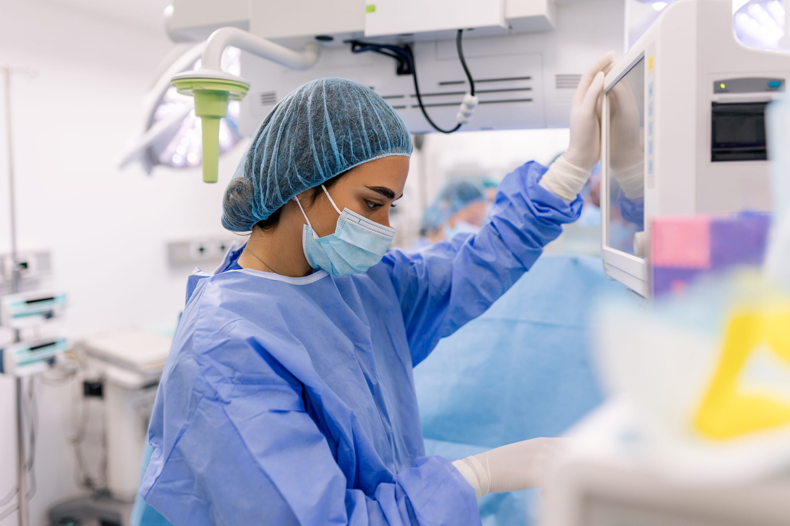 Operating room nurse monitoring medical equipment while assisting during a hospital surgical procedure.