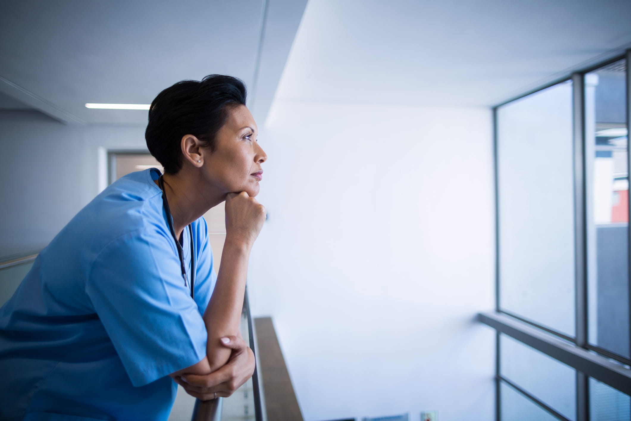 Nurse standing by a hospital window, thoughtfully looking out into the distance.