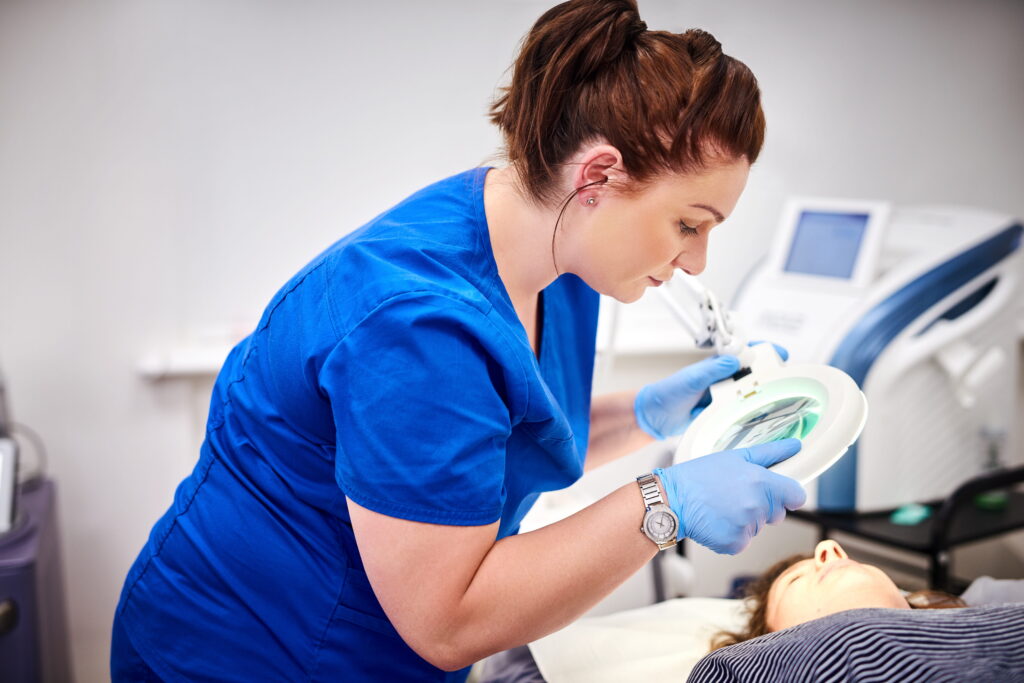 Aesthetic nurse examines a patient using a magnifying lamp during a cosmetic treatment.