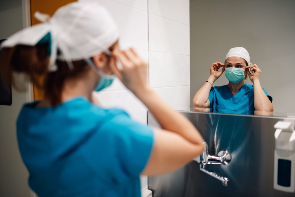 Nurse adjusts a protective face mask while preparing for patient care.