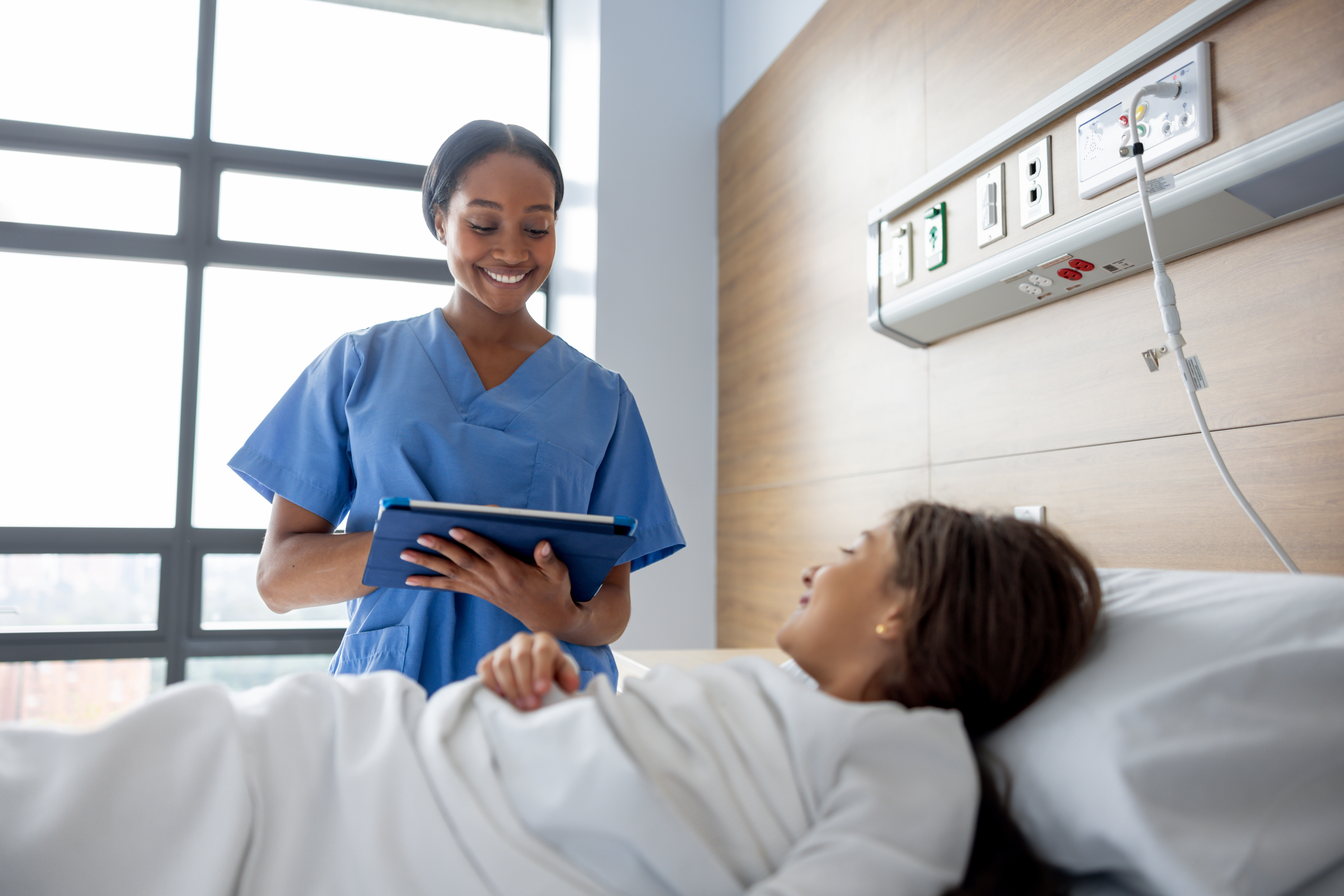 Happy nurse checking a medical record while visiting a girl in bed at the hospital