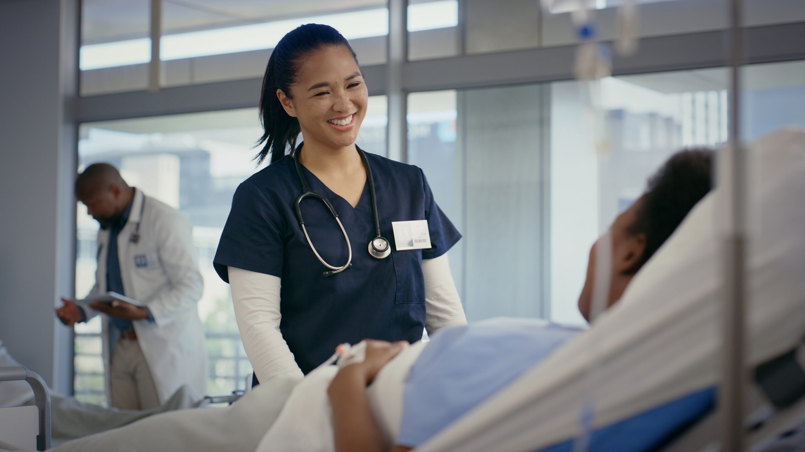 Healthcare, nurse and smile in hospital with patient for checkup, feedback or wellness. Consulting, happy and medical with employee speaking to woman in bed at clinic for diagnosis or treatment